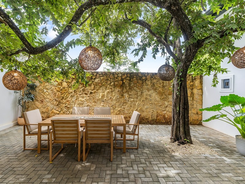 A walled courtyard with a mature tree, woven pendant lights and a teak table for six