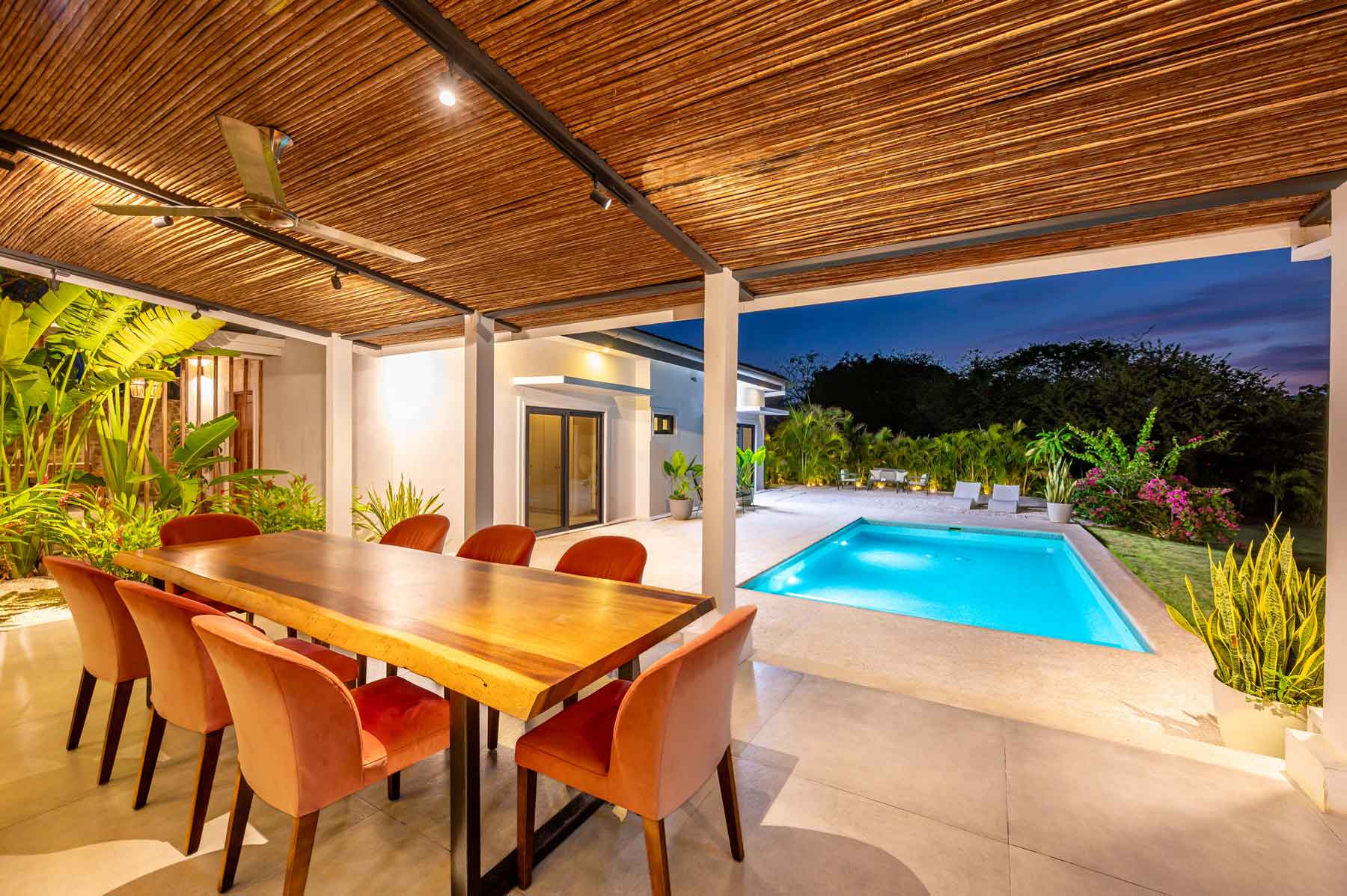 The covered terrace with a live-edge dining table for ten beside the lit pool